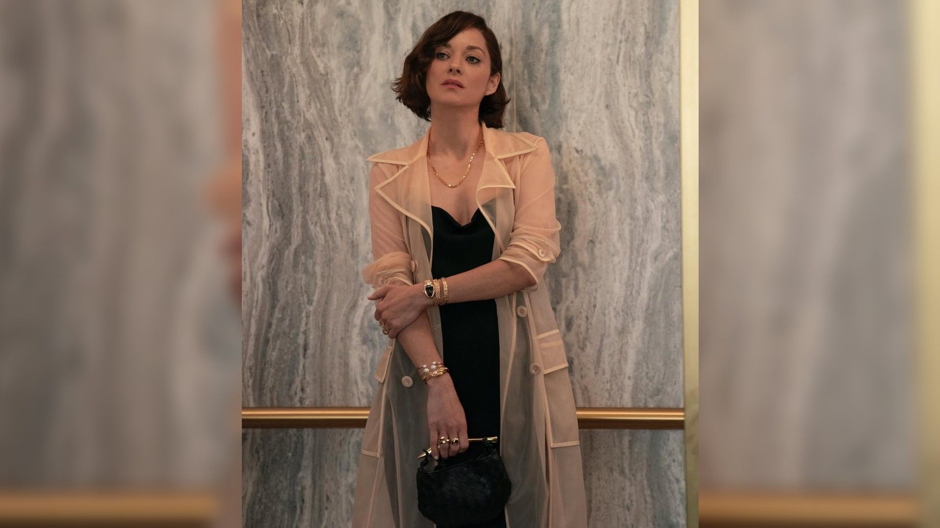 Марион Котийяр в деловом образе стоит на фоне стены, кадр со съемок сериала "Утреннее шоу"