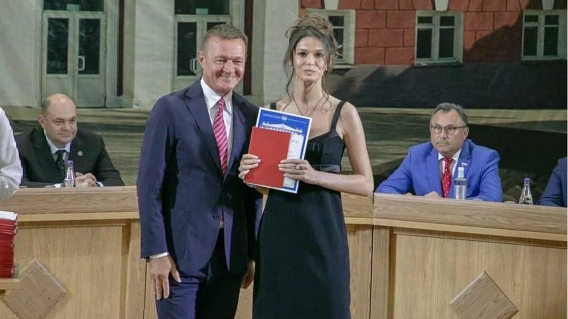 Полина Корнеева в вечернем платье на выпускном держит диплом, рядом Роман Старовойт