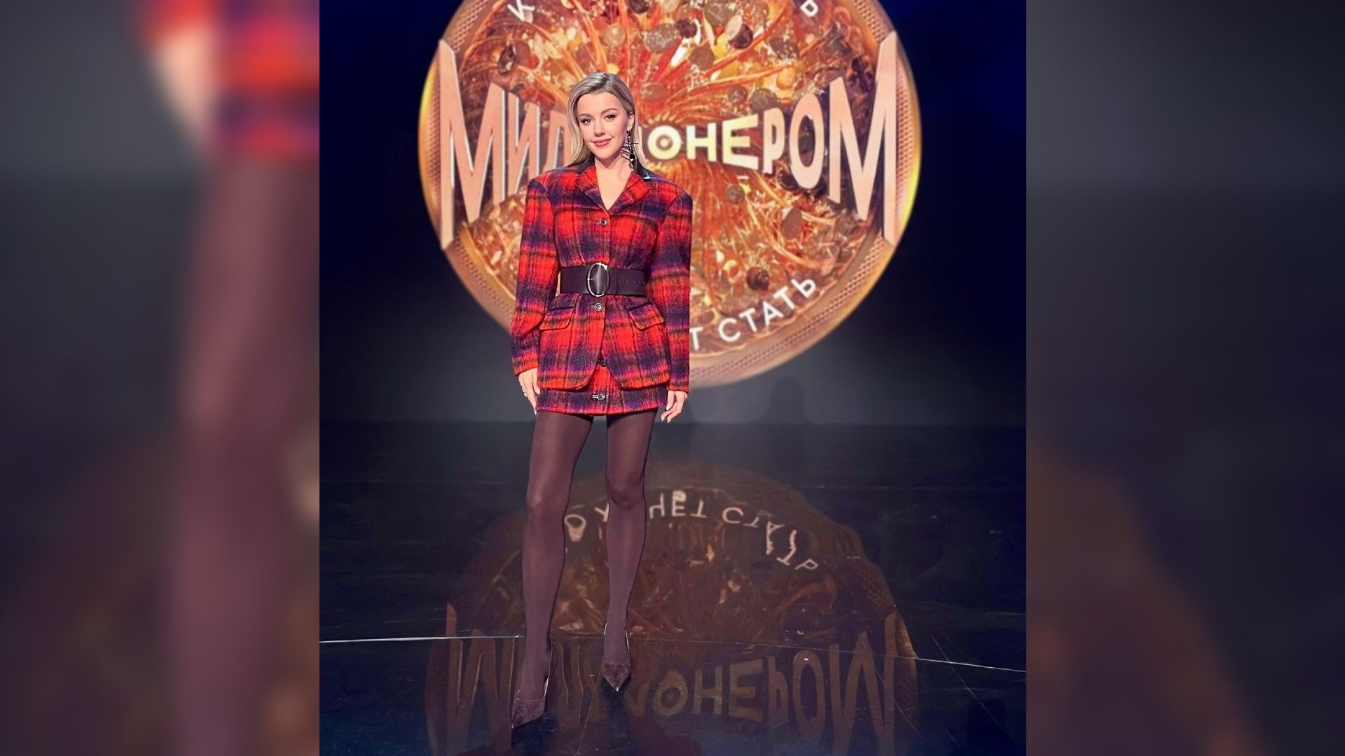 Юлианна Караулова в красном клетчатом пиджаке позирует на фоне логотипа шоу "Миллионером может стать кажд
