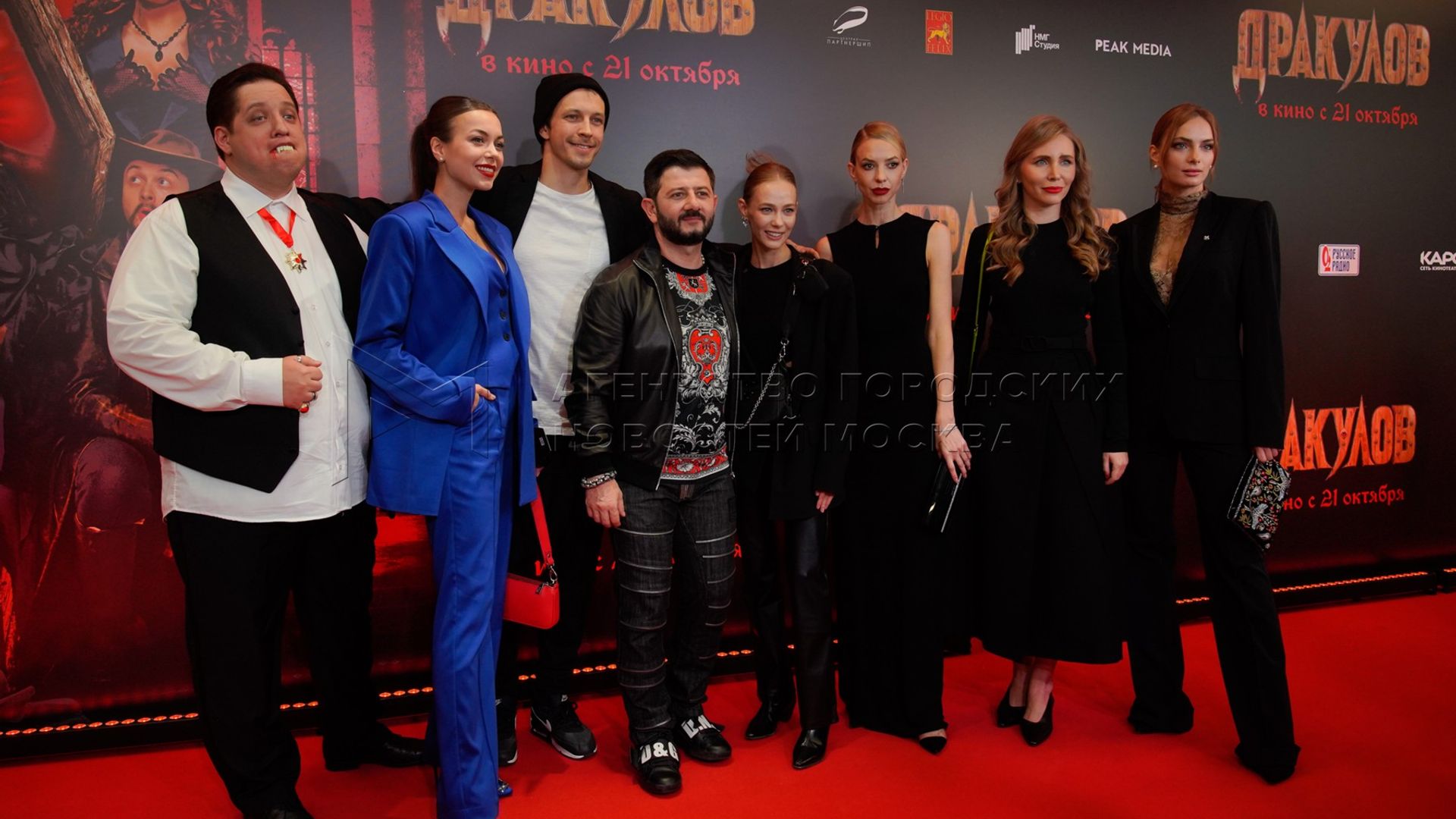 Актёры фильма "Дракулов" позируют на красной дорожке премьеры на фоне постера
