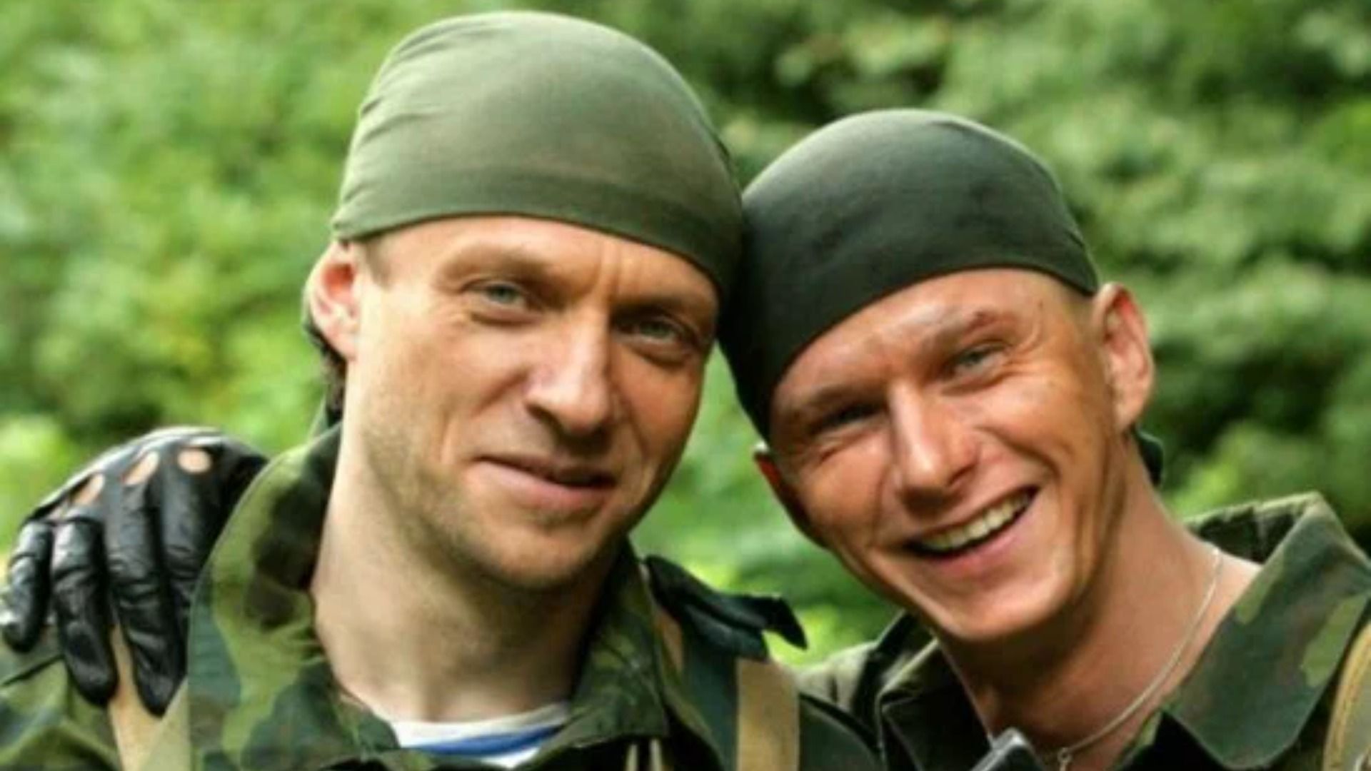 Актер Роман Курцын в бандане и военной форме обнимается с мужчиной и улыбается
