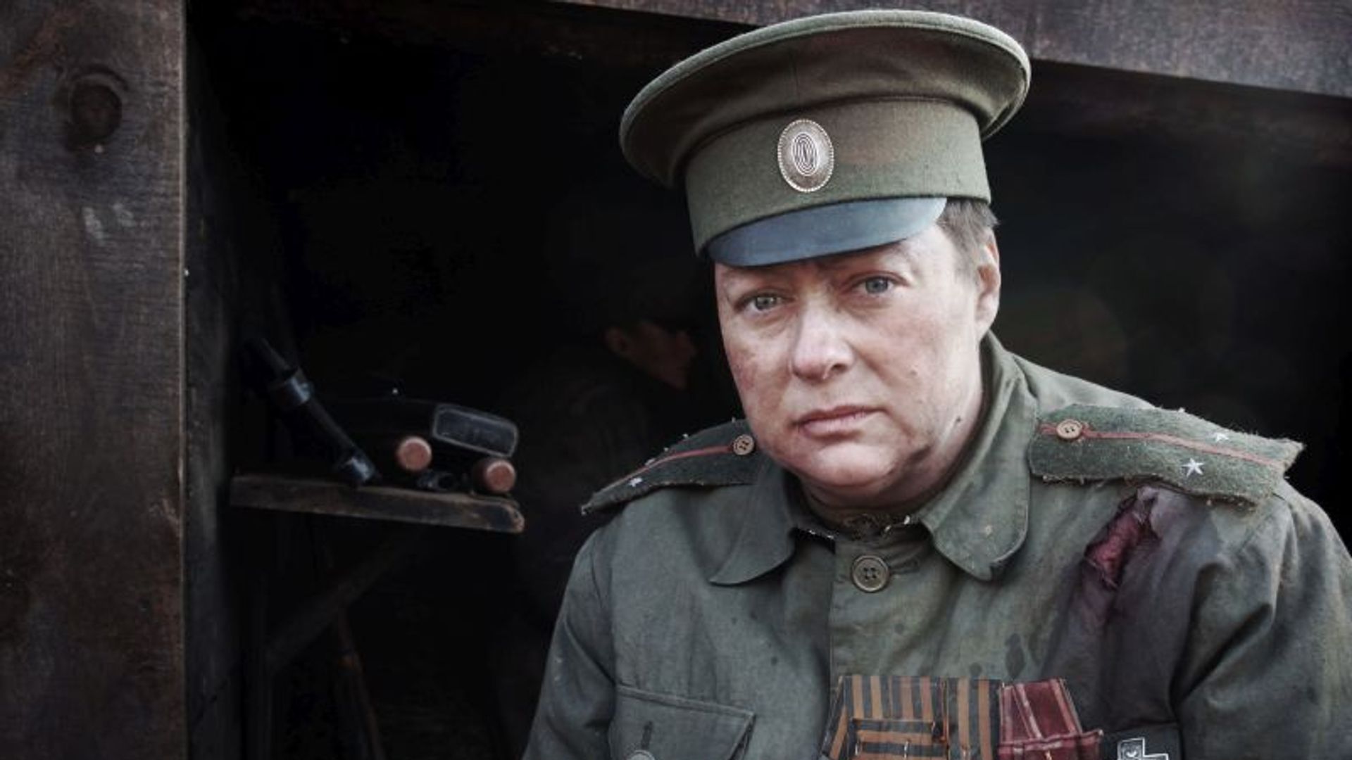 Мария Аронова в военной форме с медалями на груди сидит у входа в блиндаж, лицо усталое и суровое