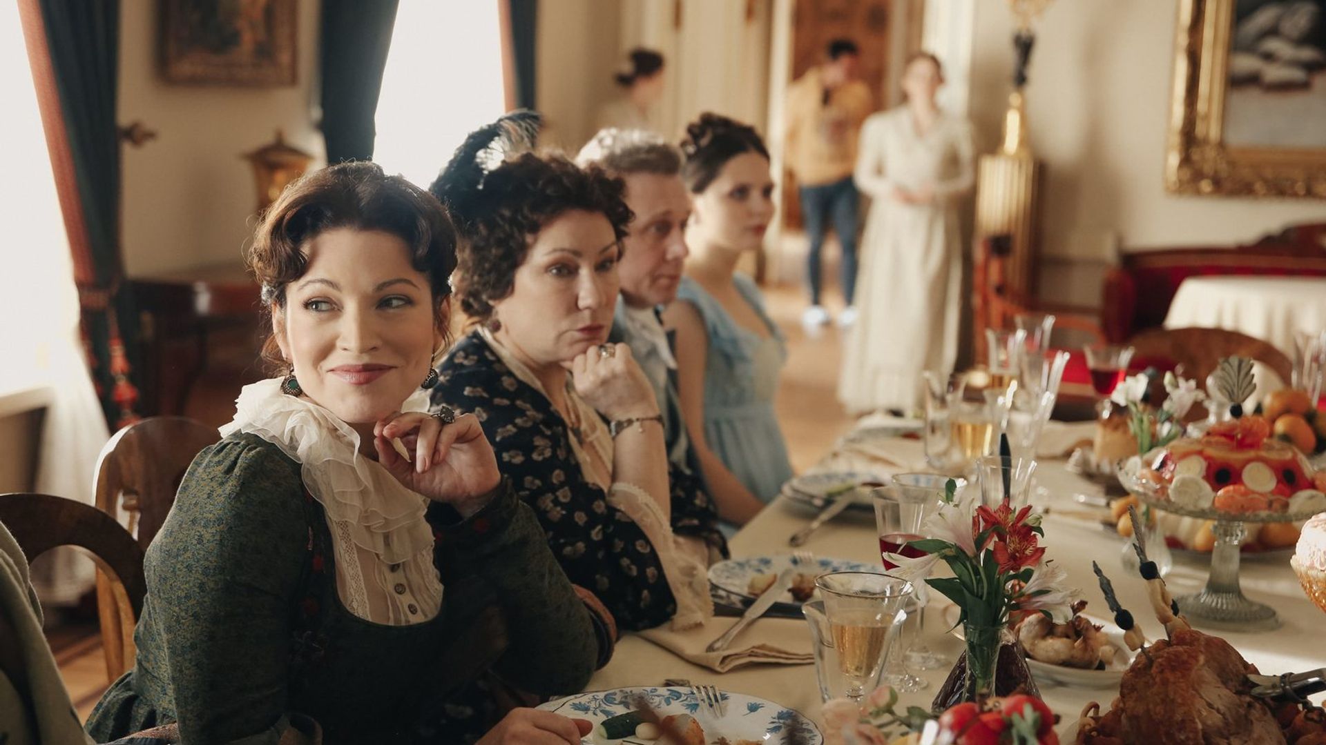 Группа женщин в костюмах начала XIX века сидит за банкетным столом