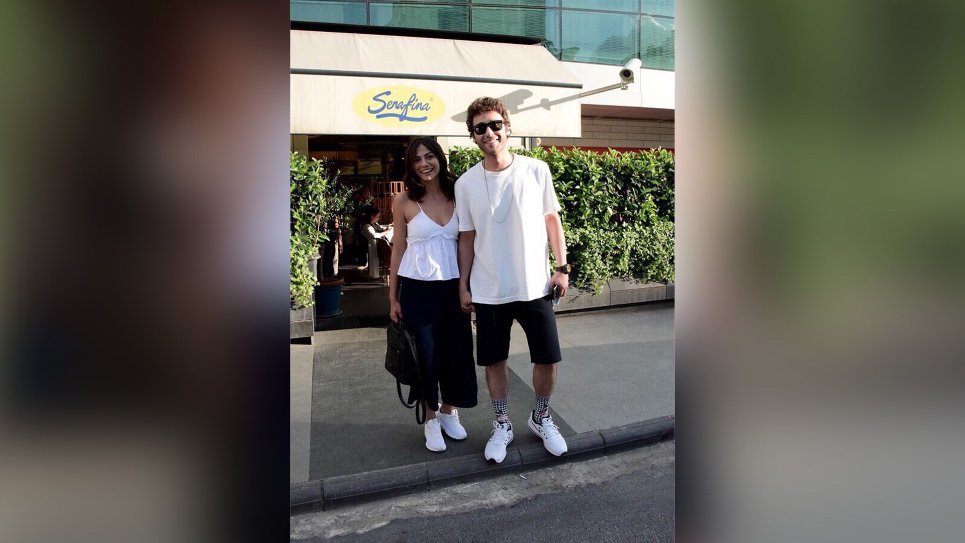 Демет Оздемир и Сечкин Оздемир стоят на тротуаре, держась за руки, и широко улыбаются