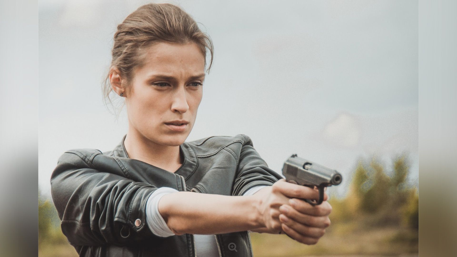 Виктория Корлякова в кожаной куртке держит в вытянутых руках пистолет