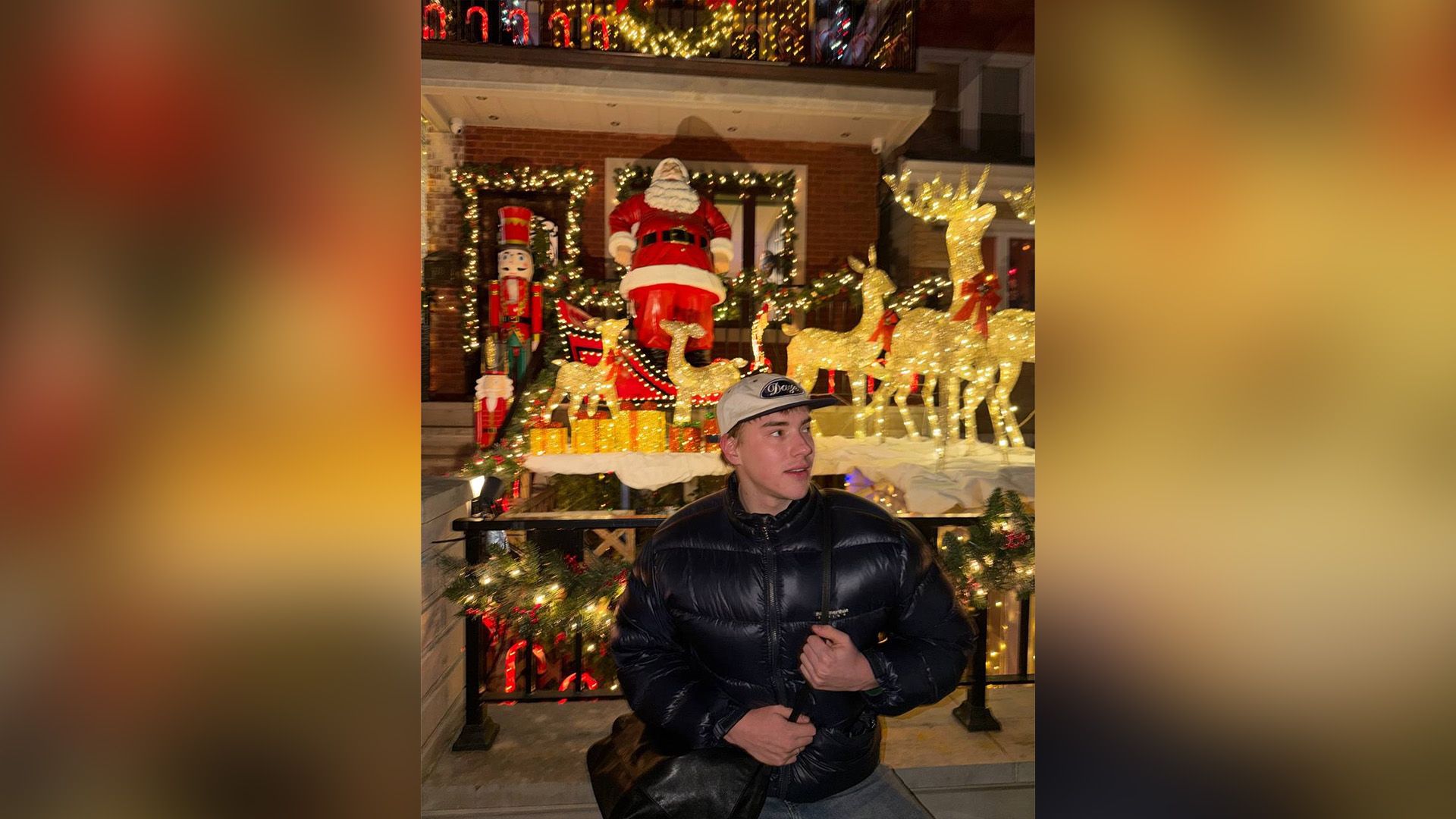 Саша Теслонд в черной куртке на фоне светящихся рождественских украшений