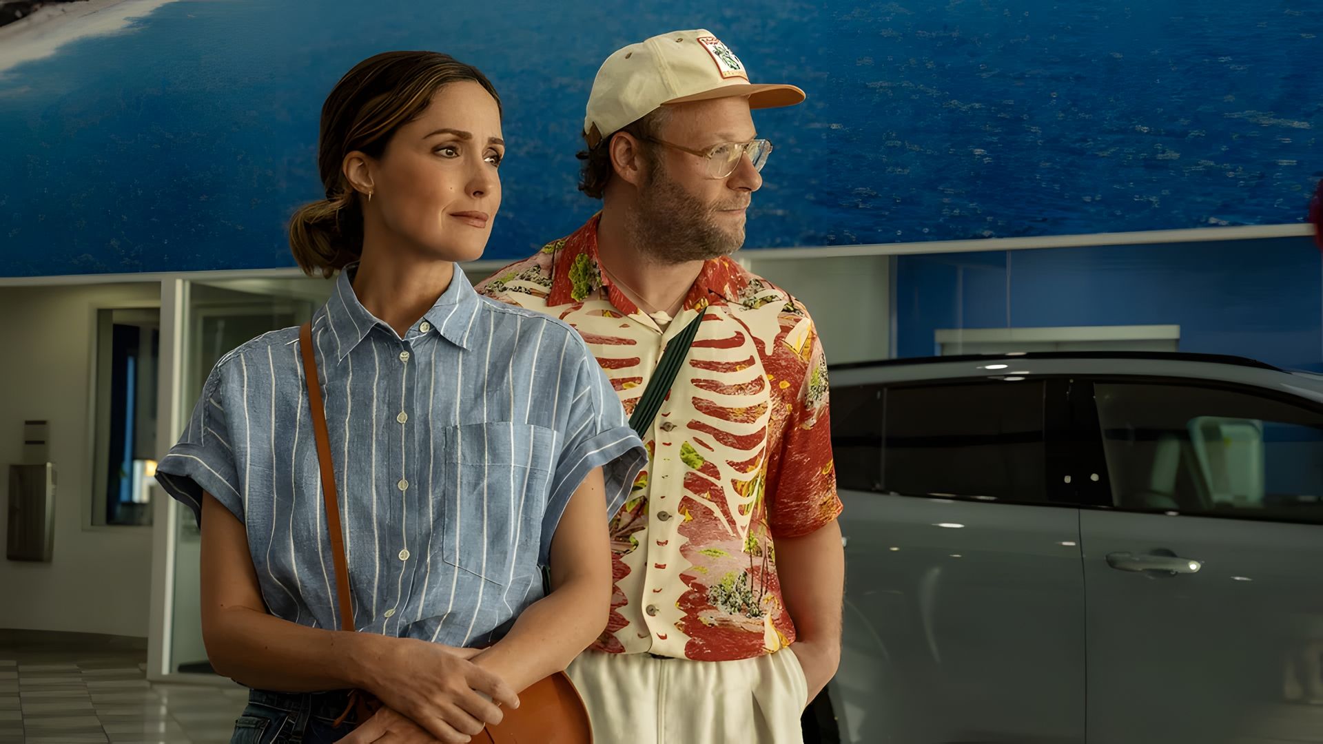 Сет Роген и Роуз Бирн в летней одежде стоят на синем фоне