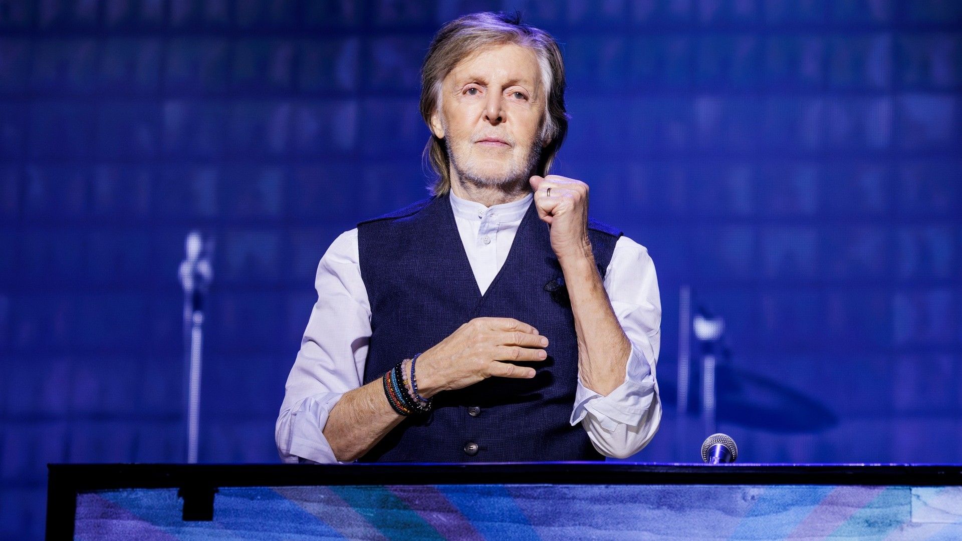 Пол Маккартни в рубашке и жилете смотрит с трибуны