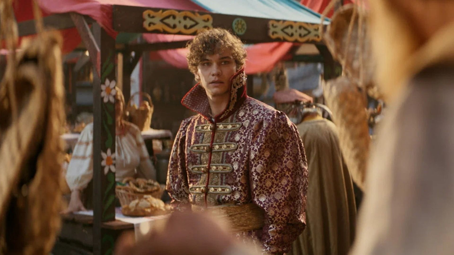 Кудрявый парень в старомодной одежде с большим воротом среди прилавков с хлебом