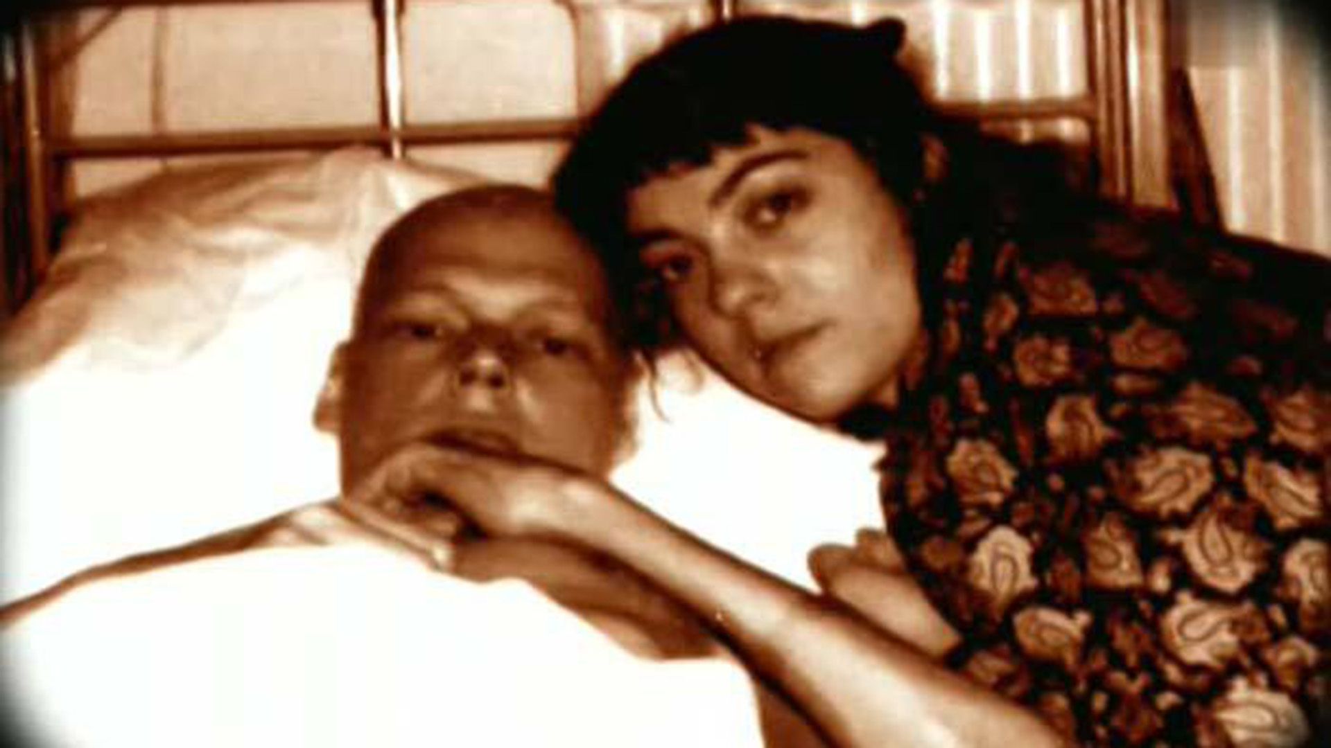 Никита Михайловский лежит в кровати, рядом сидит его вторая жена Екатерина