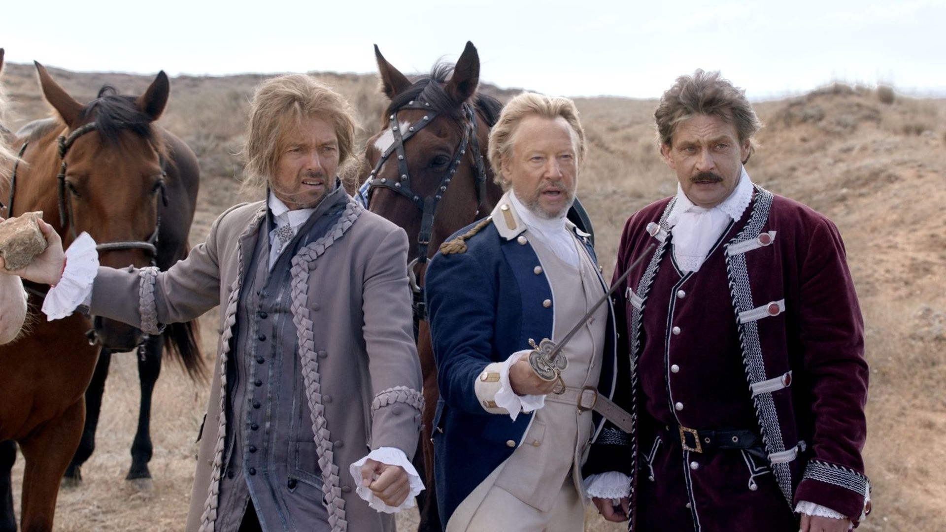 Трое мужчин в одежде русских офицеров конца XVIII века стоят на фоне лошадей