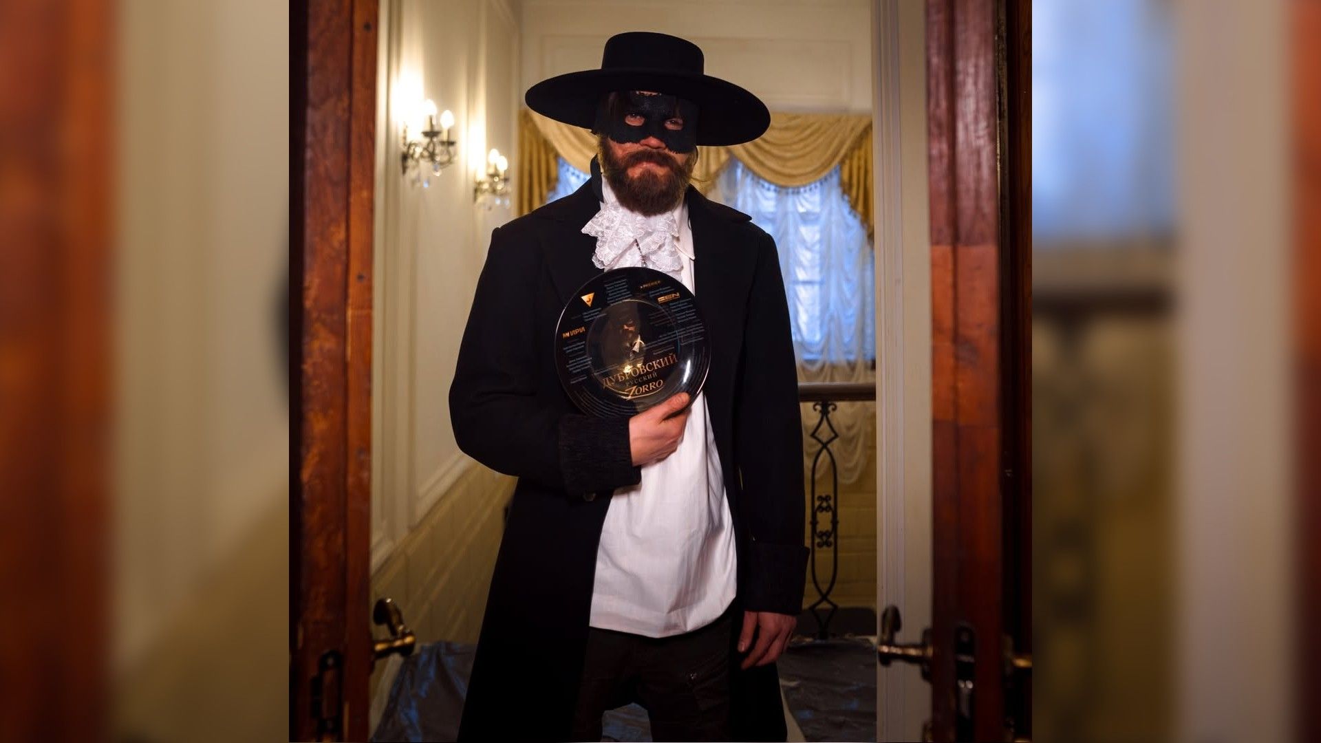 Олег Гаас в маске зорро, в шляпе и с бородой держит в руках тарелку