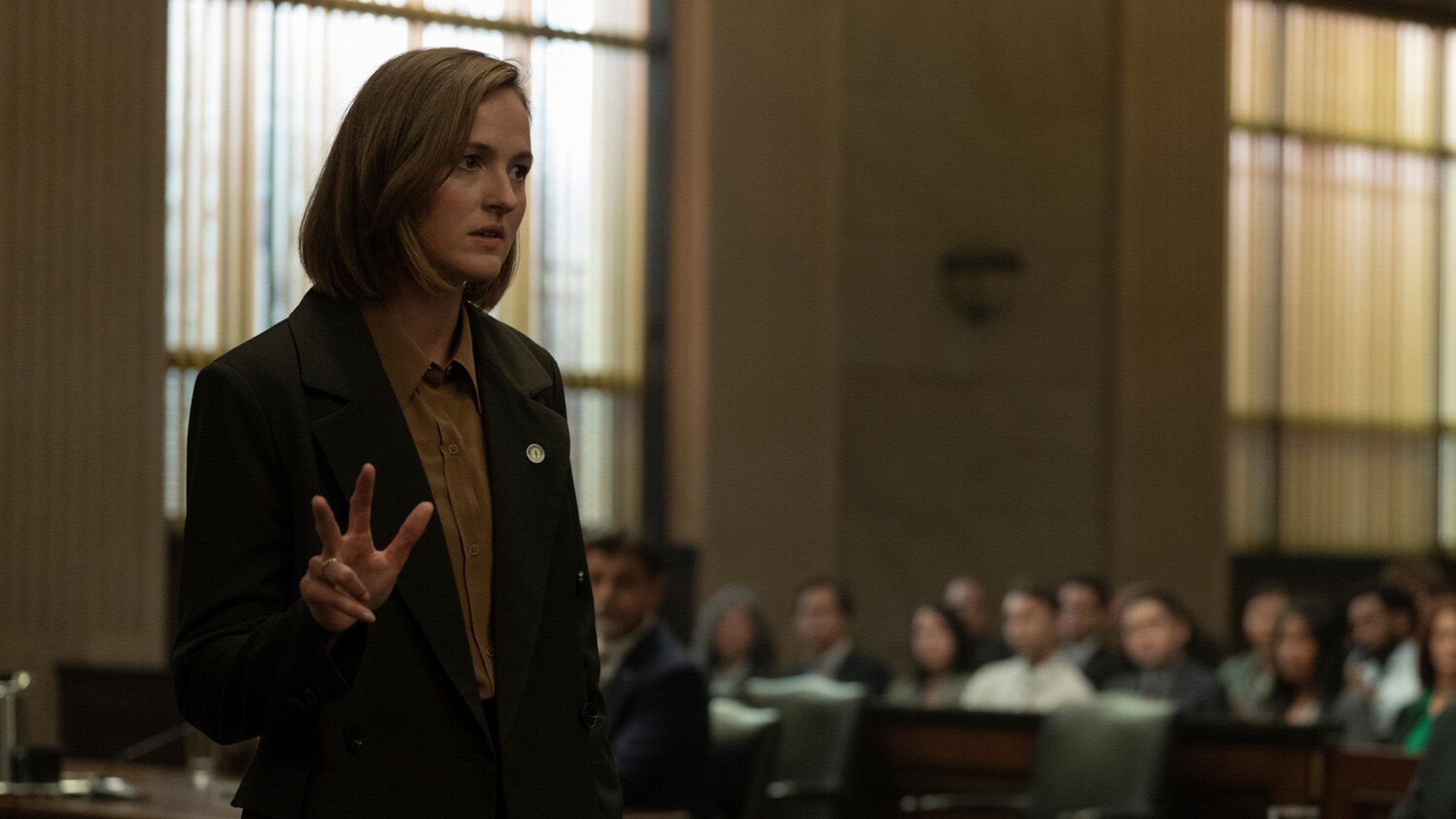 Ренате Реинсве в пиджаке стоит в зале суда и показывает пальцами число "три"