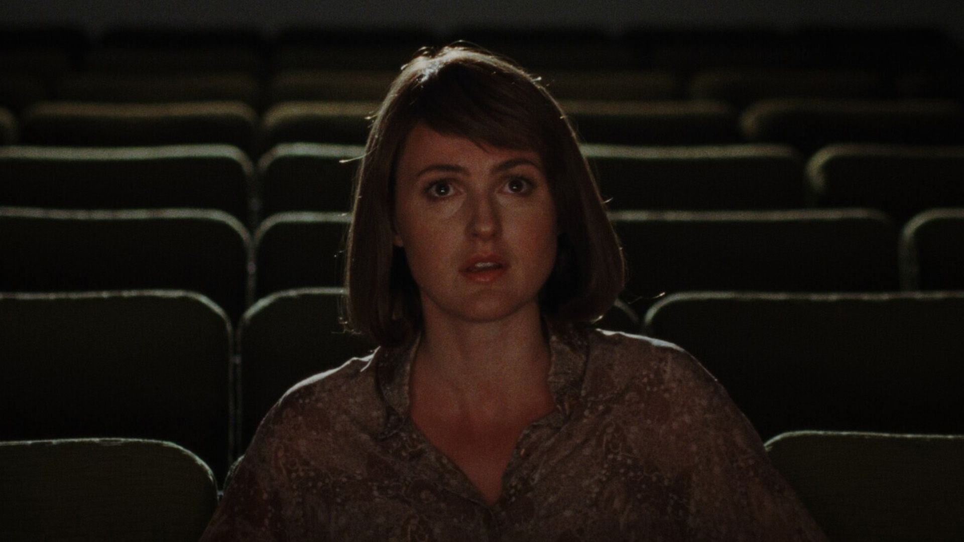 Ренате Реинсве с удивленным лицом сидит в тёмном и пустом зрительном зале