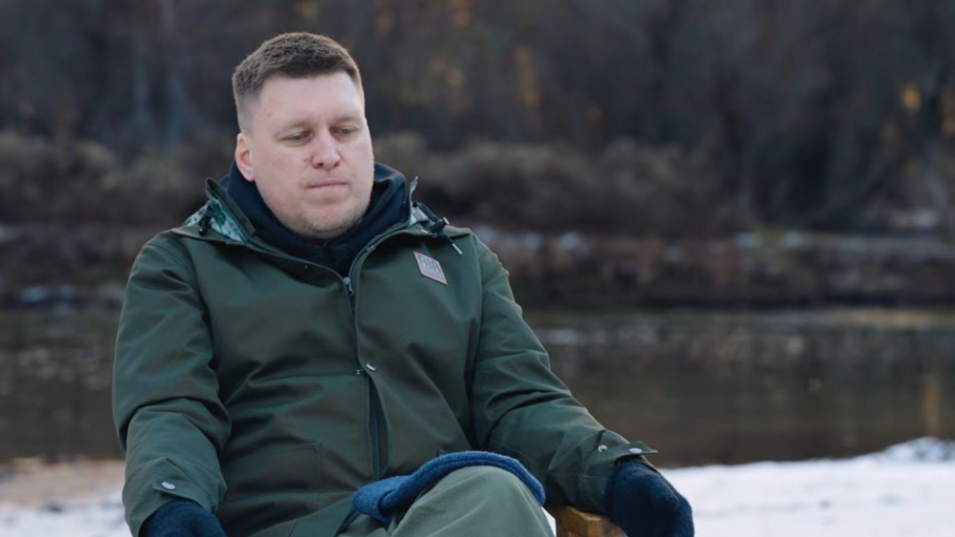 Александр Незлобин в зимней одежде сидит на фоне снега