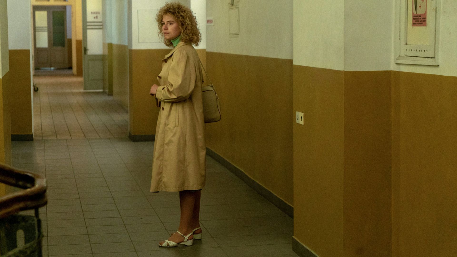 Джесси Бакли, одетая в бежевый тренч и белые босоножки, стоит в пустом коридоре больницы