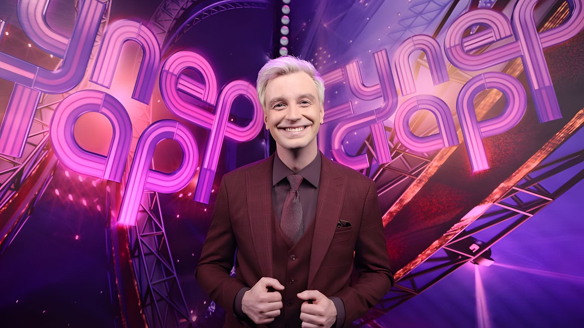 Алексей Гоман стоит на фоне надписи Суперстар и широко улыбается