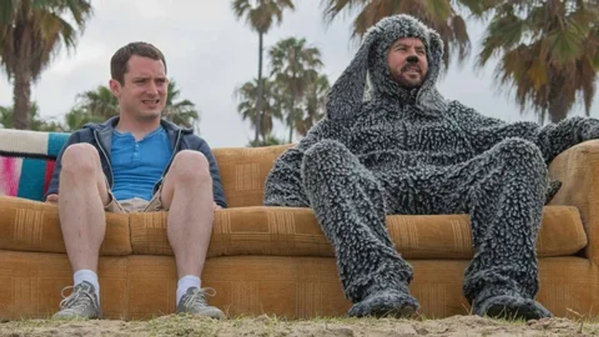 Элайджа Вуд и мужчина в костюме собаки сидят на диване на улице