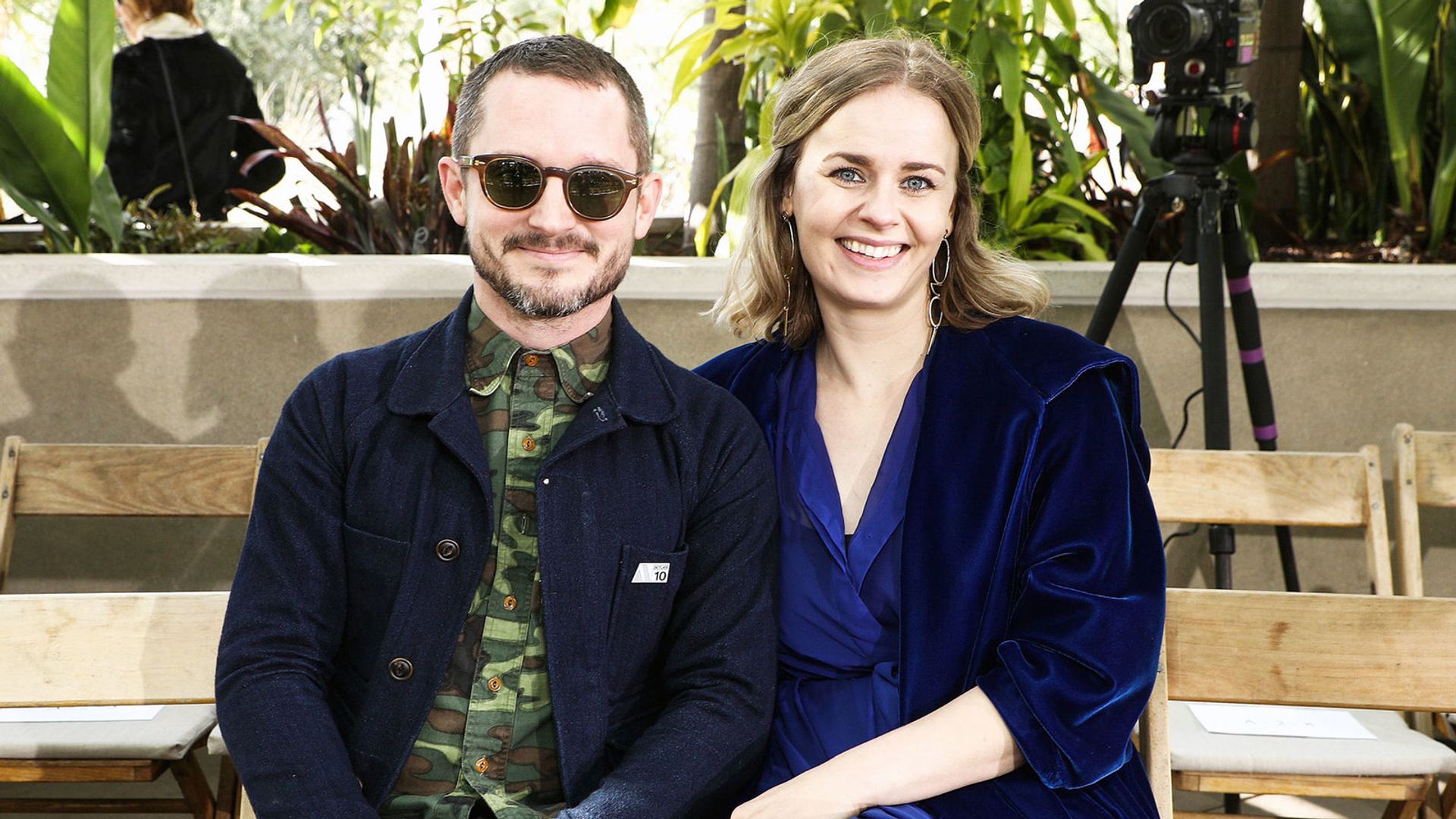 Элайджа Вуд с темных очках и Метте-Мари Конгсвед сидят вместе и улыбаются