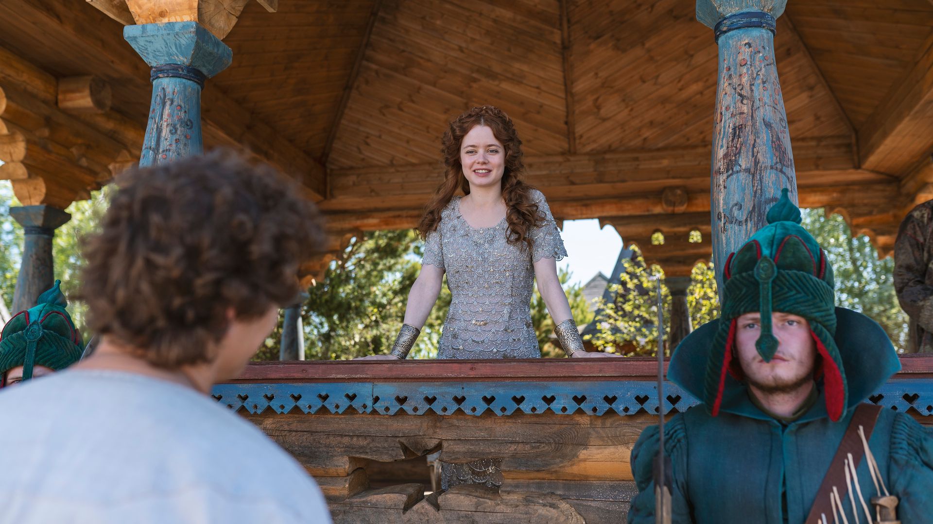 Мила Ершова в древнерусском платье смотрит вниз, стоя в резной беседке