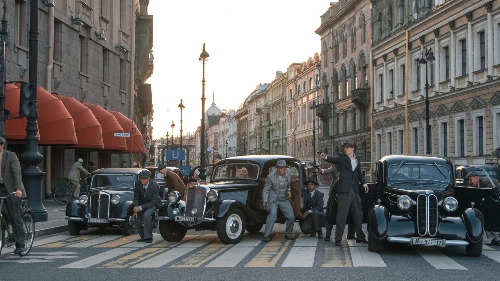 Кадр со съемок сериала "Берлинская жара", на котором актеры стоят с пистолетами у машины