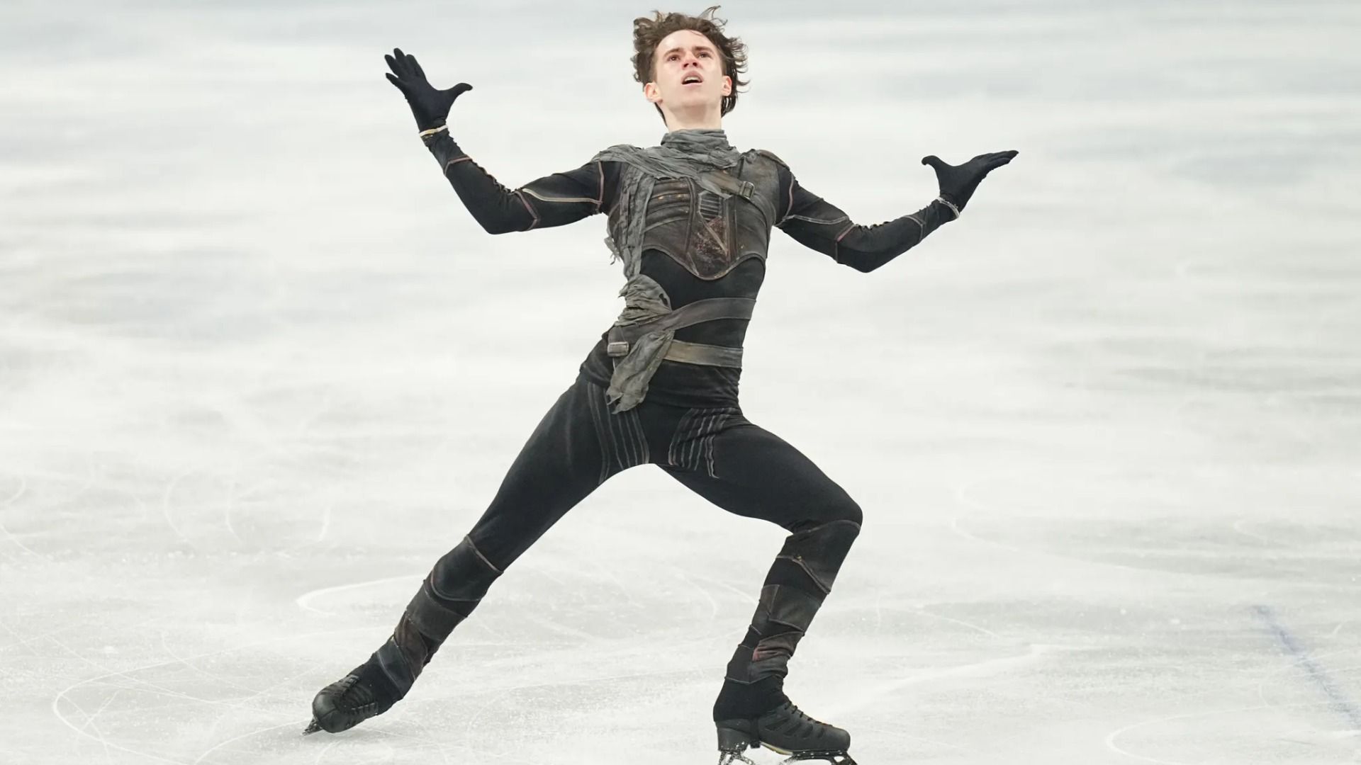 Фигурист Михаил Шайдоров в черном костюме выступает на льду на Олимпиаде-2026